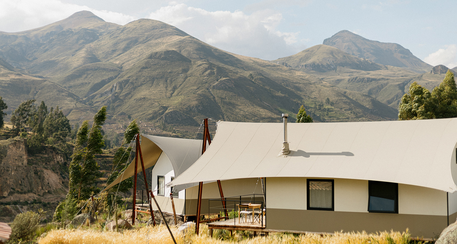 PUQIO Tented Resort in Southern Peru, photo of exterior showing white tented roof on a sunny field with mountains in the background