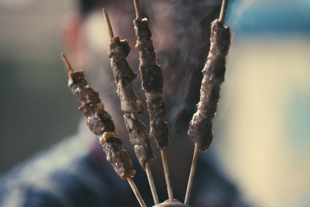 a man holds four sticks with meat