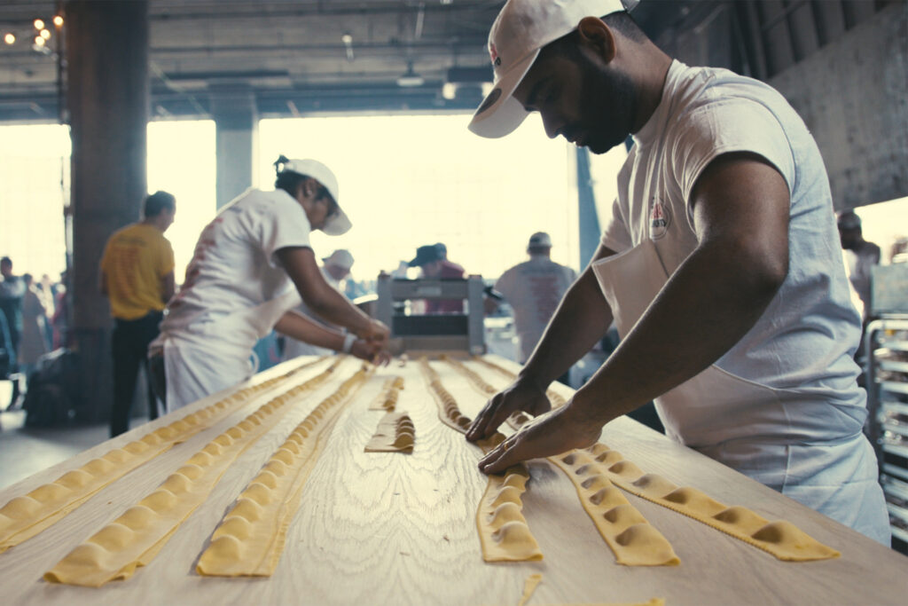 A man shapes pasta noodles on a table for Sagra di Toronto Food Festival.