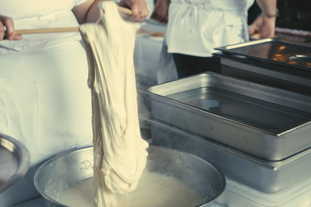 close-up view shows pasta dough, falling down above a steaming bowl of water