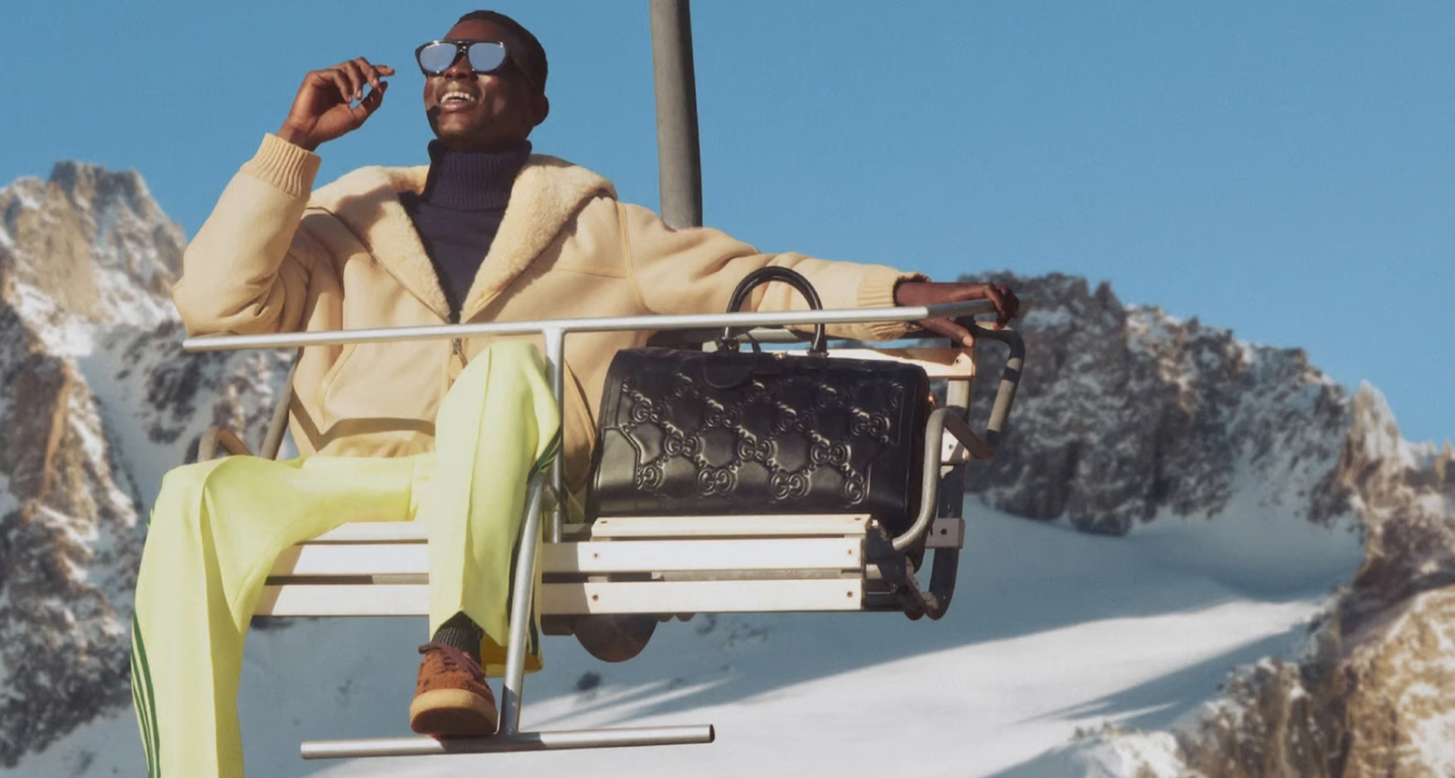 Man sitting on a ski life, dressed in apres-ski style, with mountains in the background