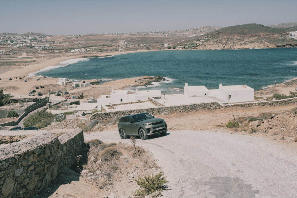 a range rover suv drives up a dirt road with blue ocean in the back, heading towards Range Rover House Mykonos Greece Aegean Sea