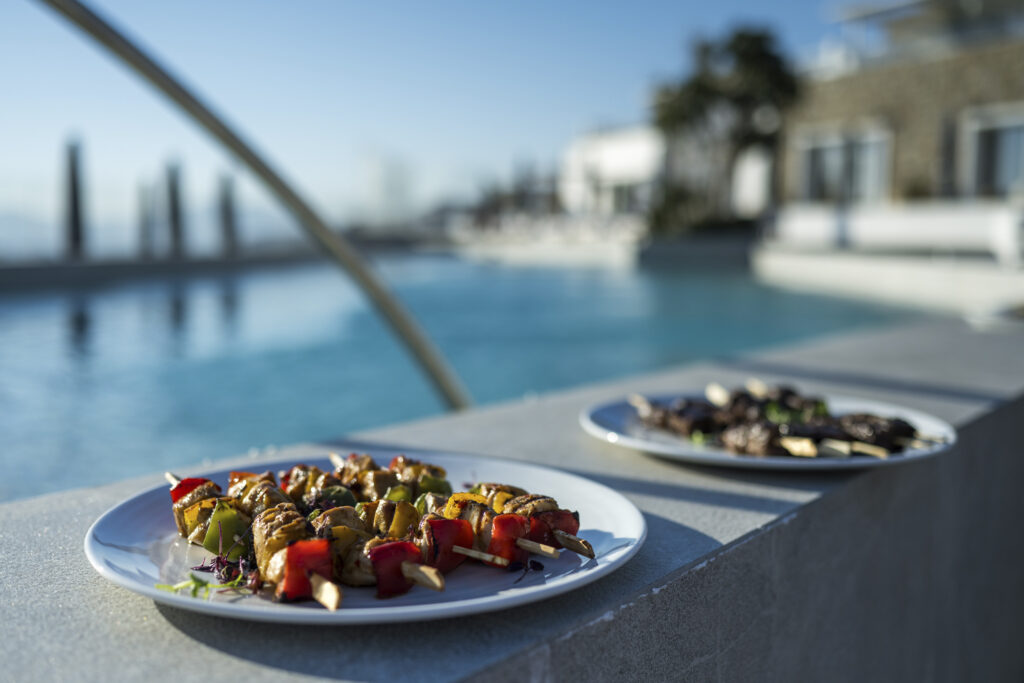 Range Rover House Mykonos Greece Aegean Sea. Food is served on two white plates atop a counter overlooking a pool