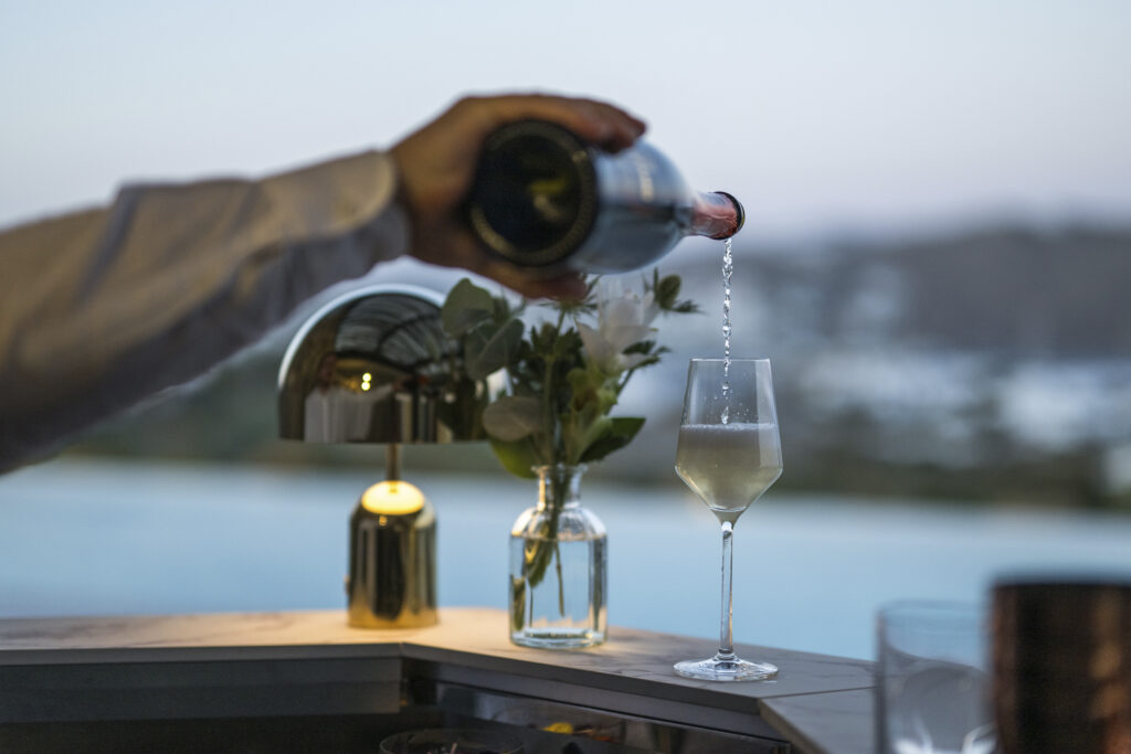 someone pours white wine into a cup overlooking a pool in the background