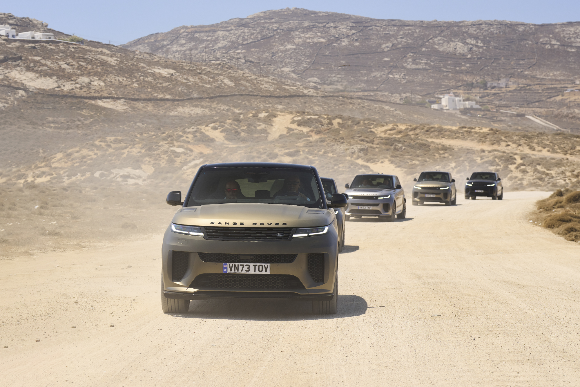 a line of range rovers drive up a dirt road