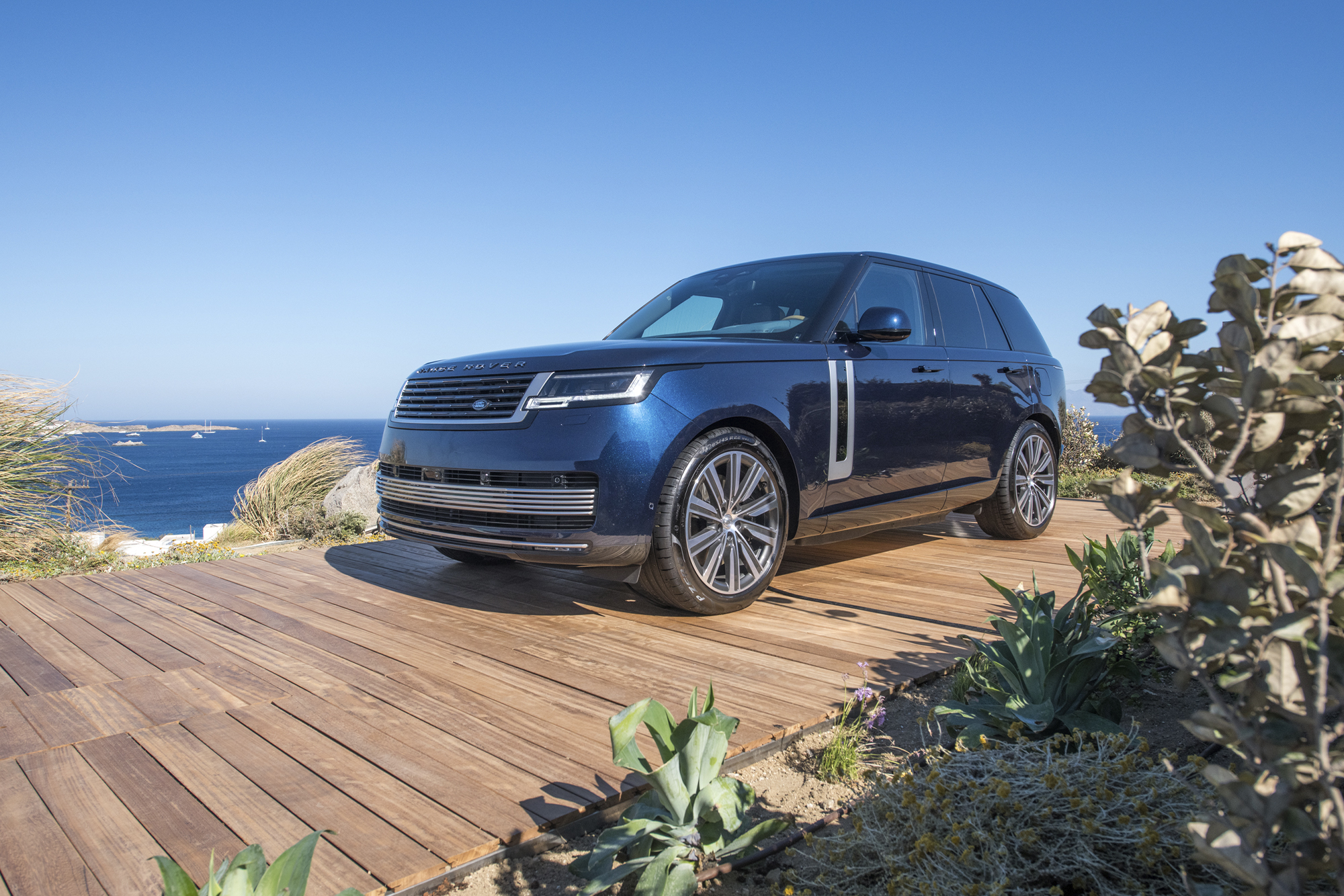 a blue range rover parked outside on a wood deak, with a blue sky and ocean in the background