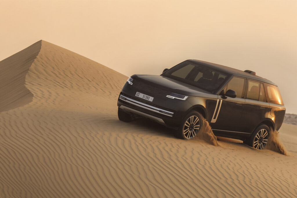 Range Rover Electric driving over a desert dune, shot from front 3/4