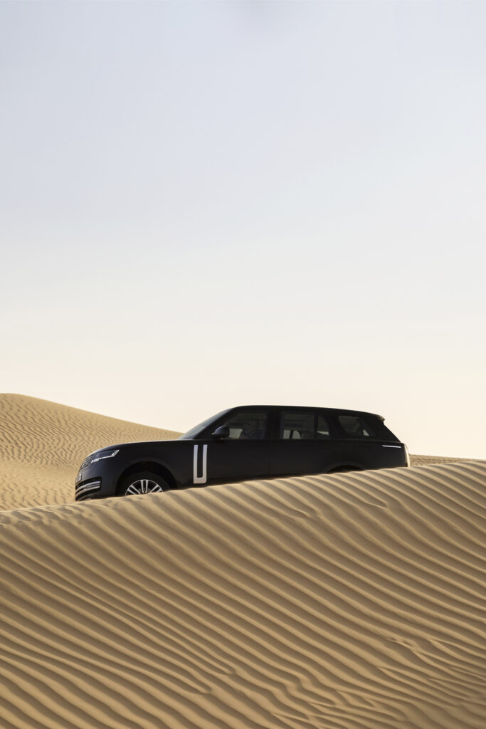 Range Rover Electric driving over combed desert sands, profile