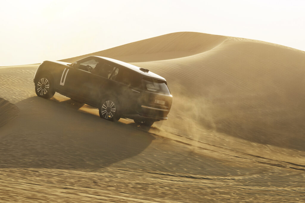 Range Rover Electric driving over dune, shot from back