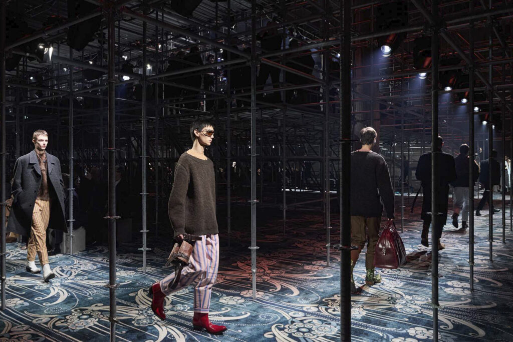 Prada Men's Fall Winter 2025: final runway walk shows a line of models walking through a nean corridor