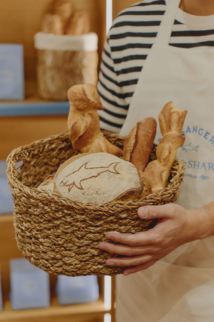 Paul and Shark Men's 2025 Collection model holds basket of bread in french bakery