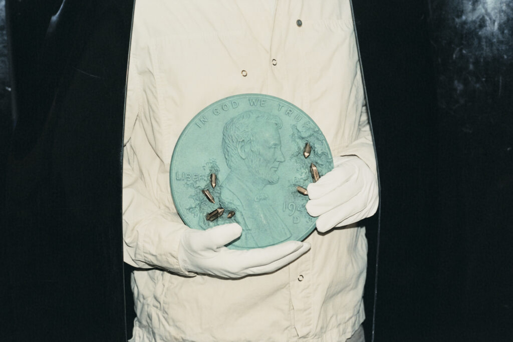 Daniel Arsham holds a large Tiffany-blue penny with white gloved hands