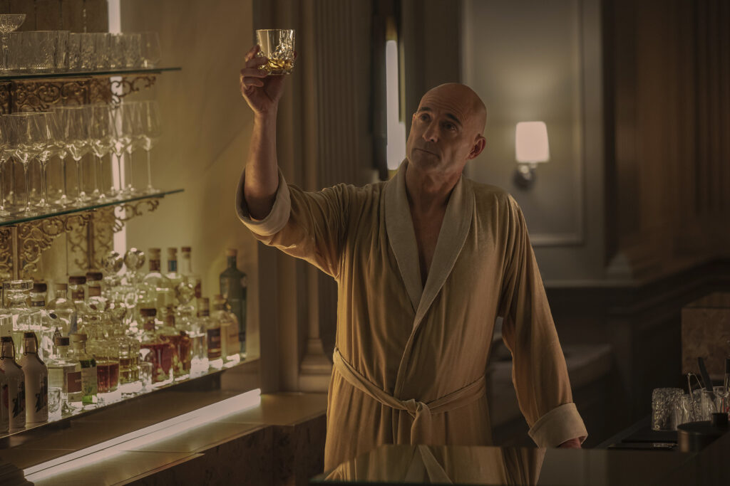 Mark Strong wears and bathrobe and raises a glass in a still from nine perfect strangers