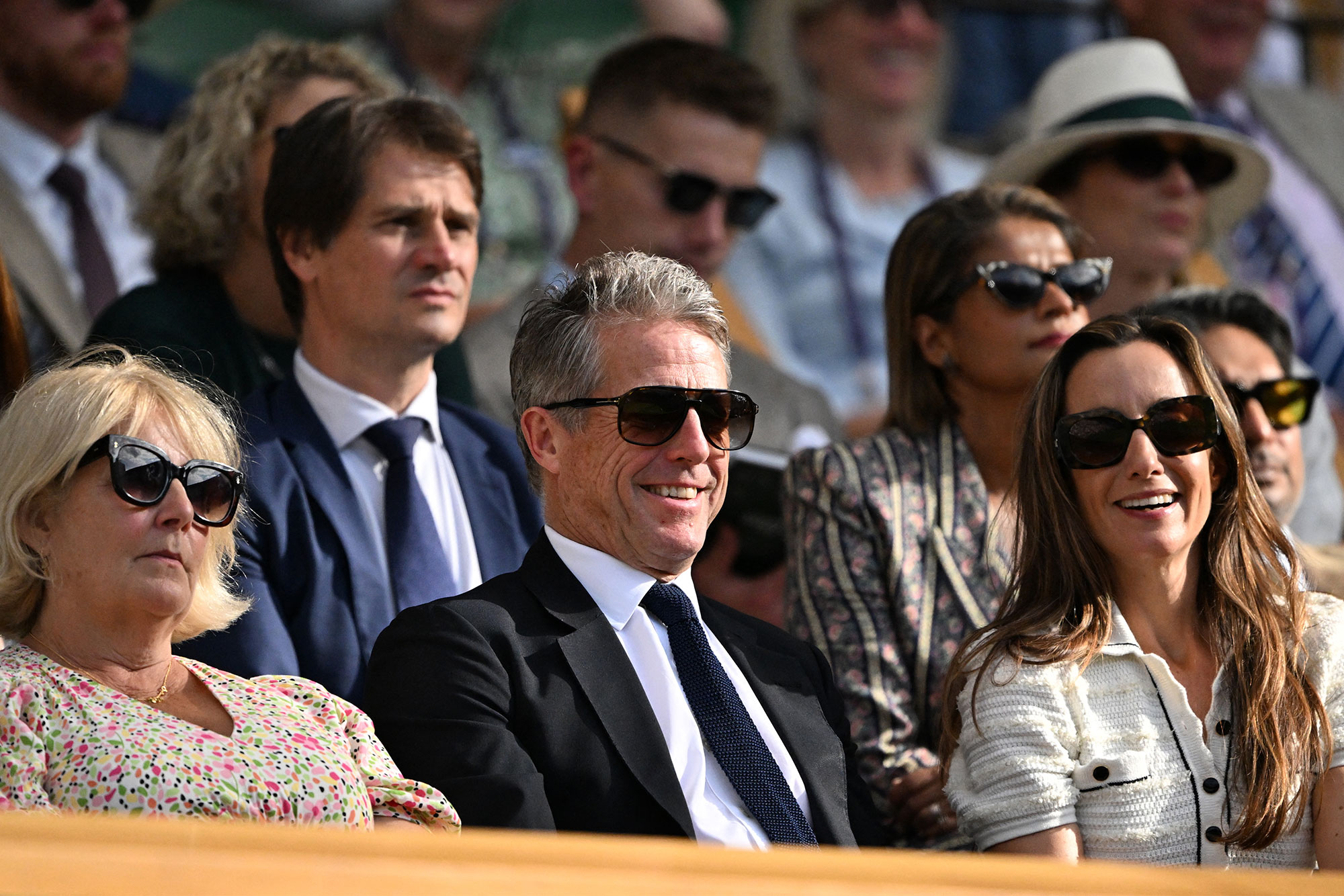 British actor Hugh Grant and his wife Swedish producer Anna Elisabet Eberstein react in the royal box of Centre Court during the men's singles quarter-final tennis match between Serbia's Novak Djokovic and Italy's Flavio Cobolli on the tenth day of the 2025 Wimbledon Championships at The All England Lawn Tennis and Croquet Club in Wimbledon, southwest London, on July 9, 2025. (Photo by Kirill KUDRYAVTSEV / AFP) / RESTRICTED TO EDITORIAL USE (Photo by KIRILL KUDRYAVTSEV/AFP via Getty Images)