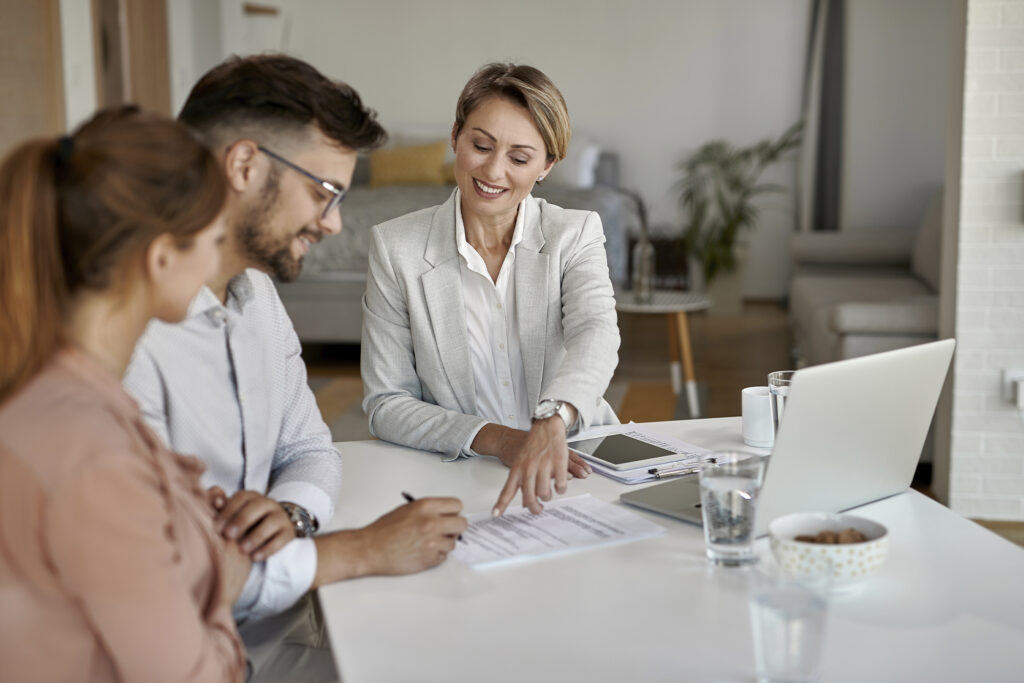 A man and a woman meet with a financial planner at a white table. Photo sourced from Adobe Stock.