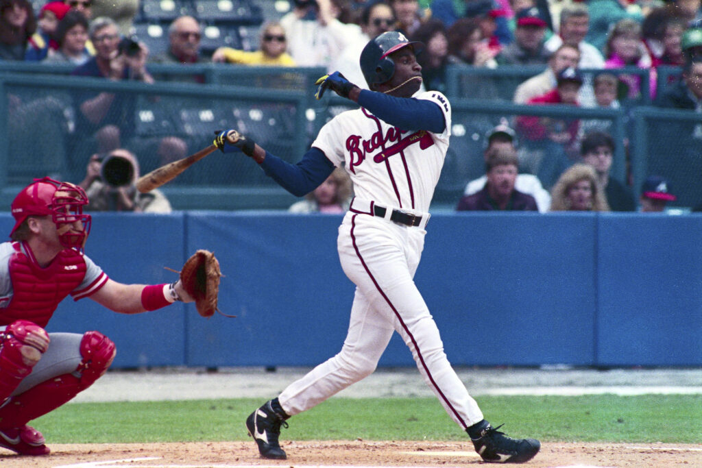 Braves' outfielder Deion Sanders (R), who is known for his flamboyant football talents, gets his necklace caught in his mouth as he slams a triple to center field in 1st inning action 4/21. Braves officials say Sanders has toned down his image and his developing into a fine baseball player. Photo by 	Bettmann / Contributor via Getty Images.