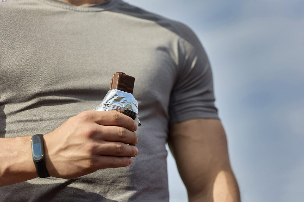 Man eats a protein bar, close up of unwrapped protein bar